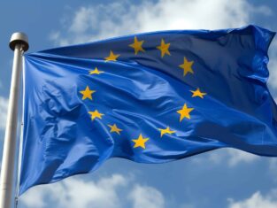 European Union EU flag on a pole waving in the wind with a blue sky on a sunny day as background